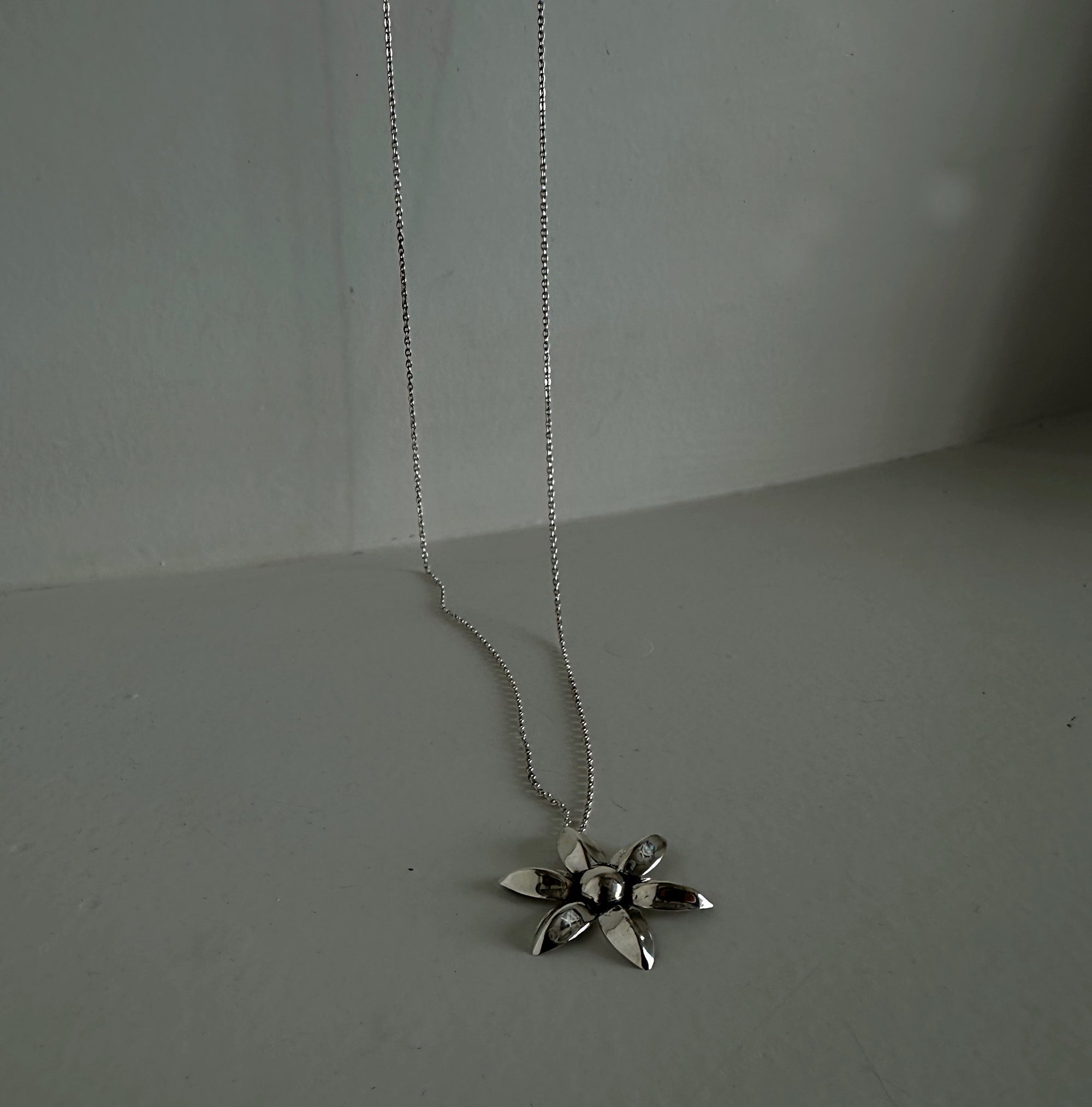 Silver flower pendant necklace on a plain background
