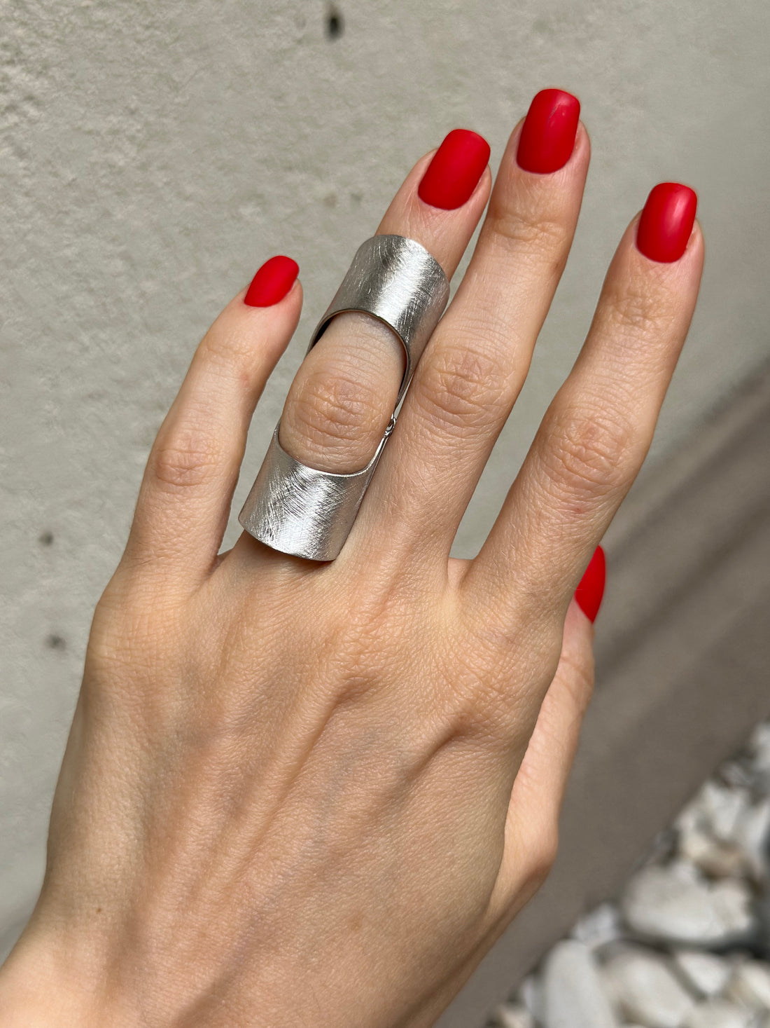 A person's hand wearing a sterling silver full finger ring with a matte finish.