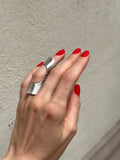 Hand with silver ring and red nails against a textured wall.