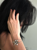 Person wearing a silver bracelet with a floral design on a neutral background