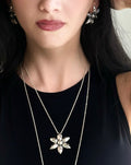 Close-up of a person wearing a silver necklace with a floral pendant on a black background