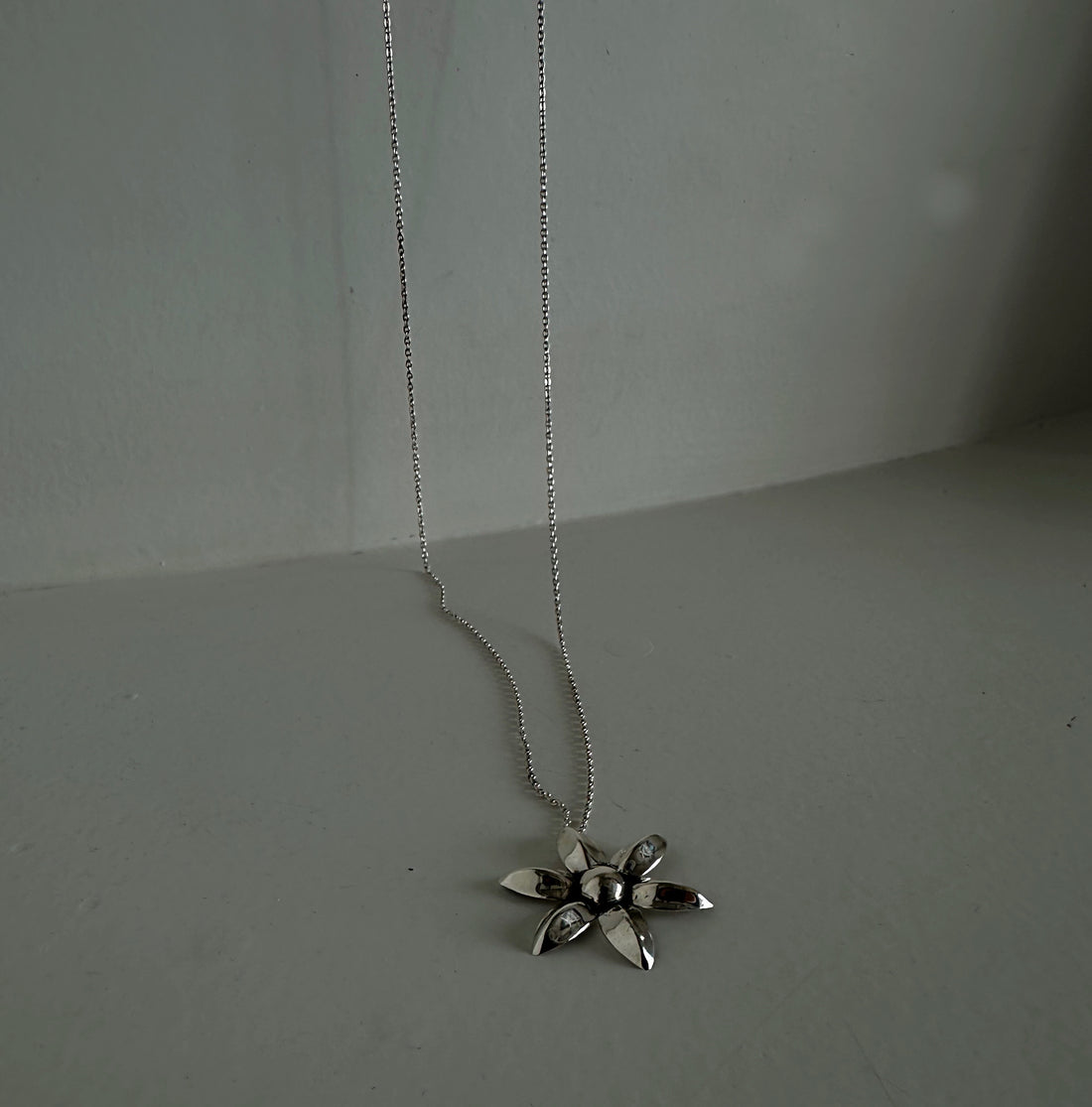 Silver flower pendant necklace on a plain background