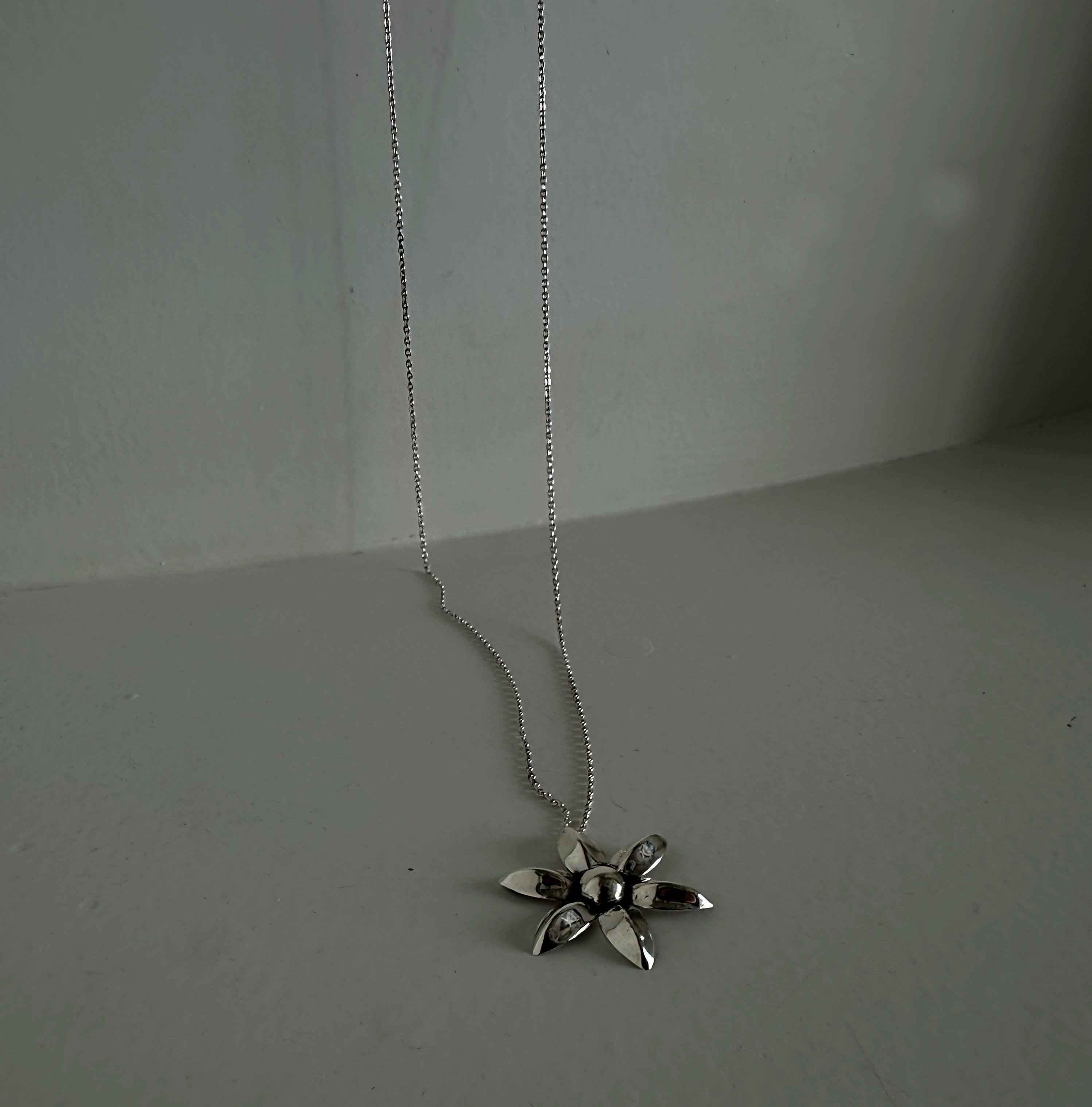 Silver flower pendant necklace on a plain backgroundslider_item_VrrRnK