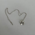 Silver necklace with a floral shaped pendant on a light gray background