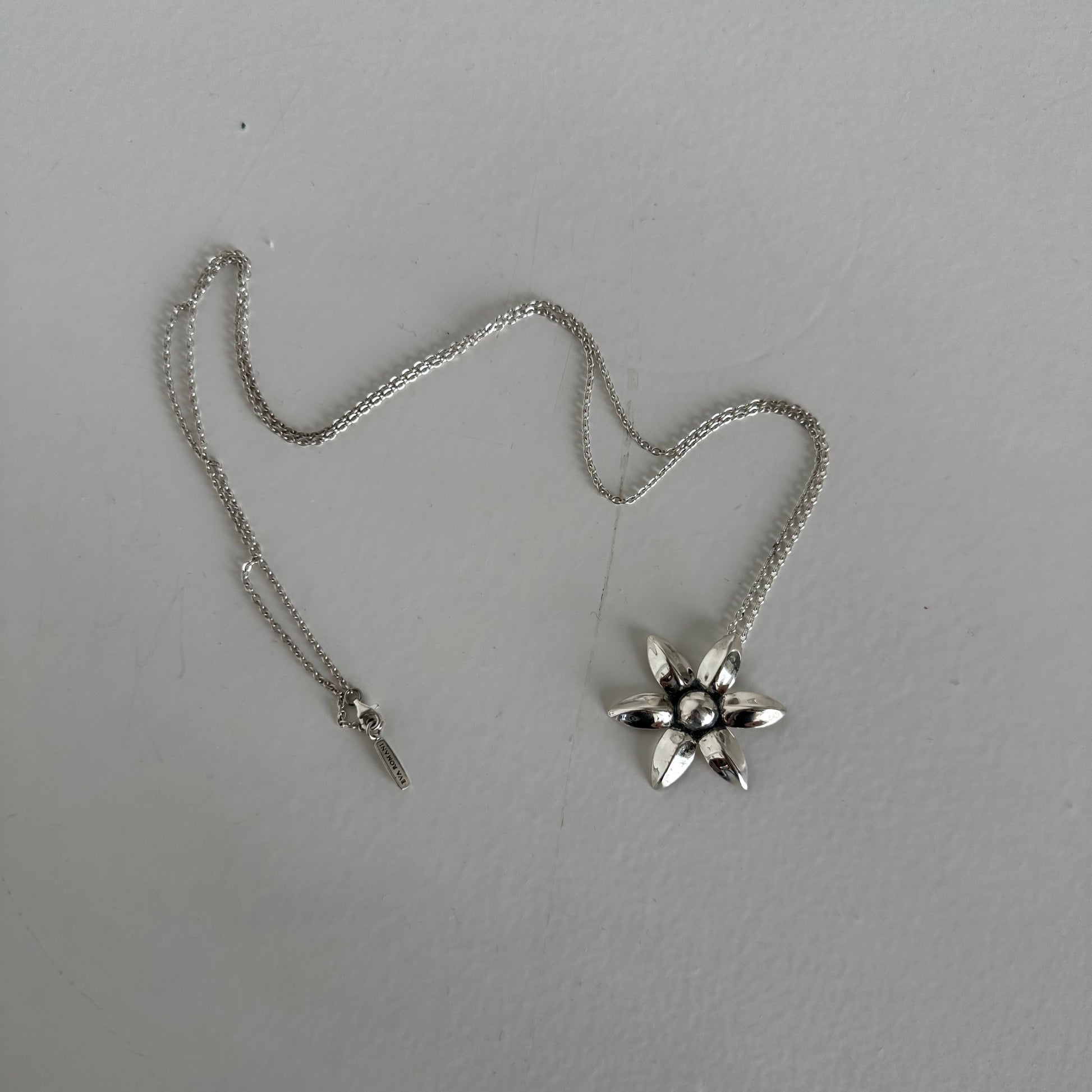 Silver necklace with a floral shaped pendant on a light gray background